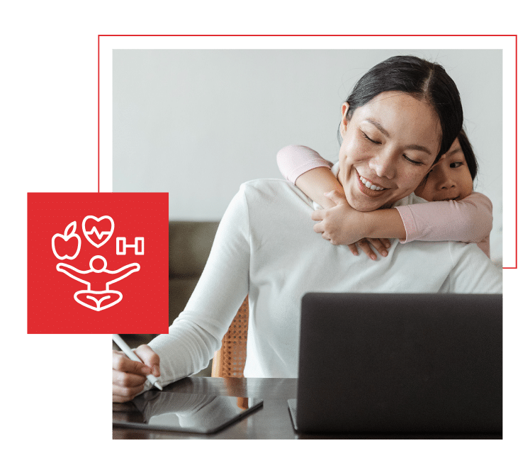 Smiling mother working on a laptop while her young daughter hugs her from behind